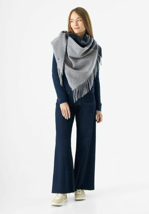 Châle en mélange de laine gris avec des bords frangés, drapé sur un haut marine. Associé à des jeans en denim foncé à jambes larges et des baskets de couleur claire.