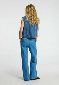 Chaleco de mezclilla sin mangas, en azul medio, combinado con pantalones de mezclilla de pierna ancha y cintura alta, que presentan una textura suave y costuras mínimas.