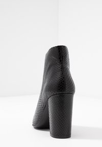 Schwarze Absatz-Stiefelette aus strukturiertem Schlangenmuster-Material, ausgestattet mit einem stabilen Absatz und einem eleganten, geschwungenen Design.