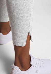 Leggings deportivos grises con un acabado texturizado, que cuentan con una cremallera lateral en el dobladillo. Llevados con zapatillas deportivas blancas.