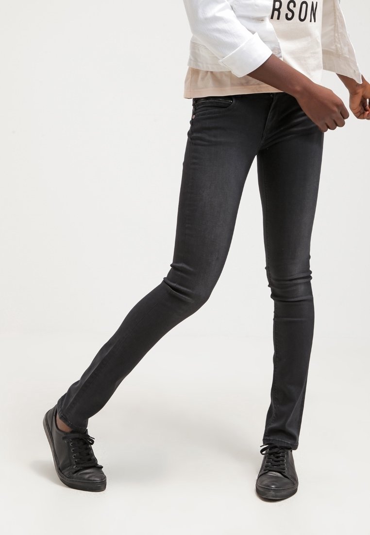 Jeans ajustados negros con una textura suave y un corte ceñido, que cuentan con bolsillos delanteros y un diseño elegante, combinados con zapatos negros de cordones.