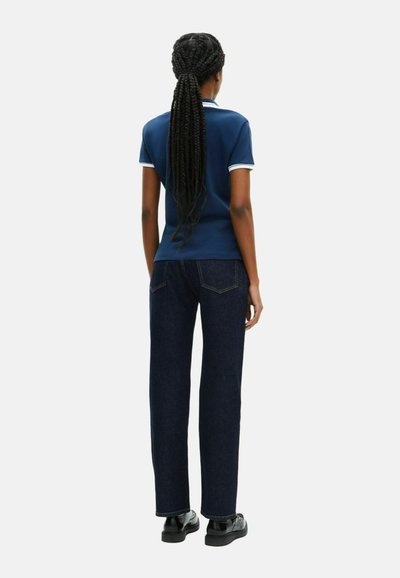 Marineblå polo med hvide accenter, parret med mørk vaskede lige ben jeans og sorte sko, set fra ryggen.