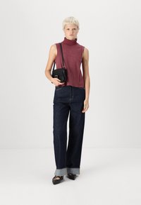 Burgundia ilma varrukat turtleneck topp koos kõrge vöökohtadega tumedast denimist laia säärega pükstega, millelt paistavad heledad denimist ääred, ning must üle õla kantav kott.