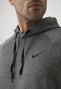 Grå hættetrøje med struktureret stof, sorte snore og et lille sort Nike-logo på venstre bryst.