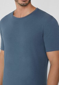Camiseta de algodón azul con cuello redondo clásico, mangas cortas y una textura suave, que presenta un corte ajustado y detalles de costura en las mangas.