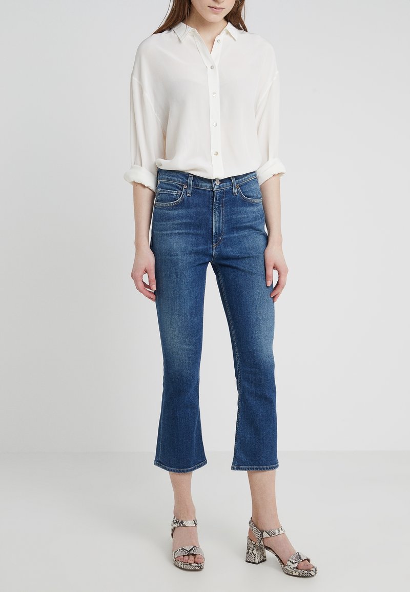 White button-up shirt with rolled sleeves, paired with blue cropped jeans and snakeskin-patterned heeled sandals. Smooth fabric and casual fit.