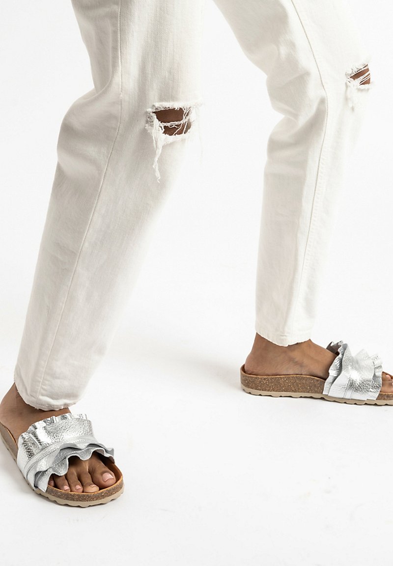 Zilveren schuifsandalen met een gerimpeld ontwerp, kurken zool en een gestructureerde afwerking, gecombineerd met witte distressed denim broek.