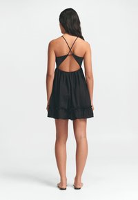 Juodas saulėgrąžų suknelė su reguliuojamais kryžminiais petnešomis, atviru nugaros dizainu ir nėriniuotu poplūdu. Lengvas audinys su minkšta tekstūra.
