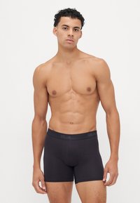 Zwarte boxershorts van een zachte, rekbare stof. Elastische tailleband met een reliëflogo. Aansluitend ontwerp en lengte tot halverwege de dij.