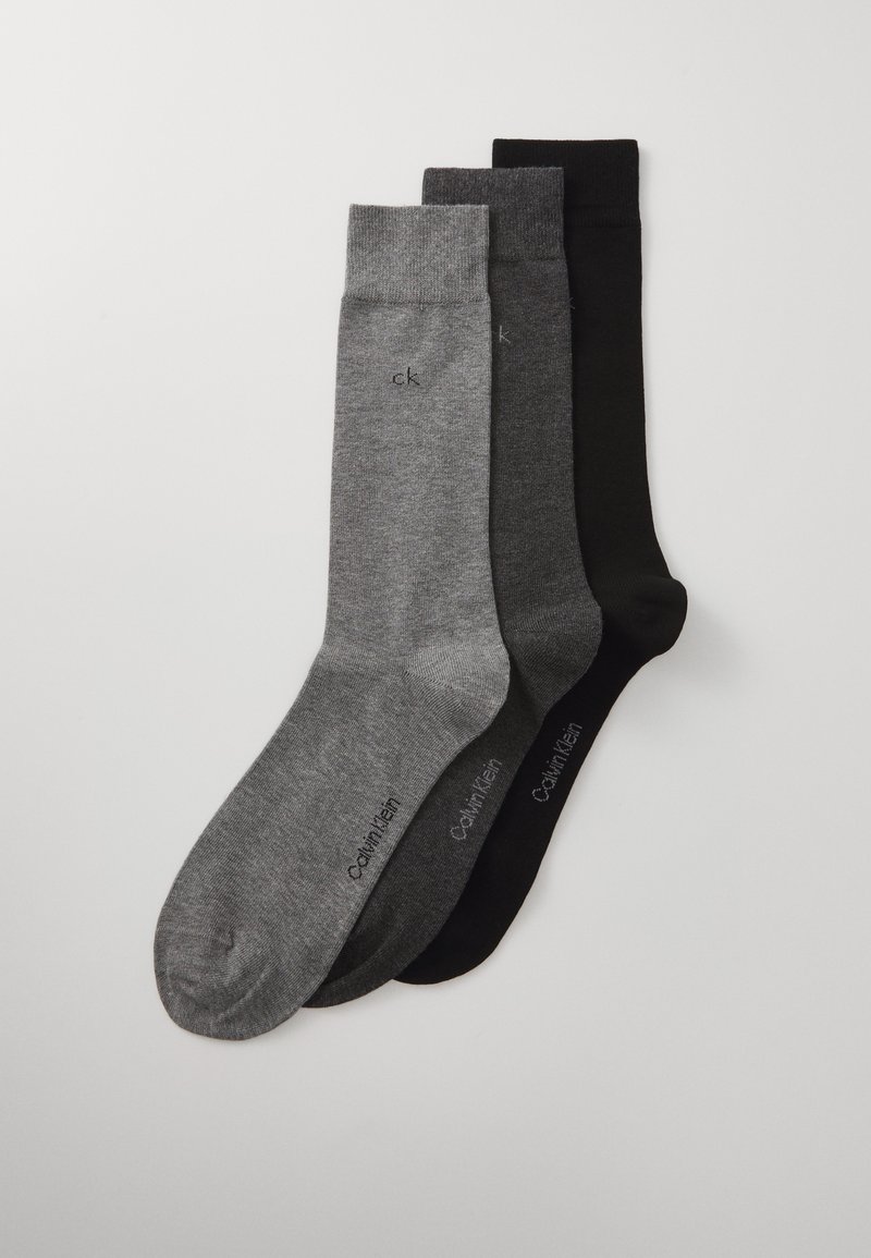 Trois paires de chaussettes en gris foncé, gris moyen et noir. Chaque paire a une texture lisse et un logo près de la cheville.