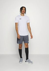 Valge lühikeste varrukatega sportlik särk musta logoga, hallid lühikesed püksid, mustad põlveni ulatuvad sokid ja hallid spordijalatsid. Sile, kerge kangas.