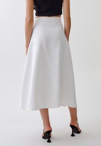 Jupe midi blanche avec une texture lisse et fluide, et une large ceinture, associée à des sandales à talons noires.