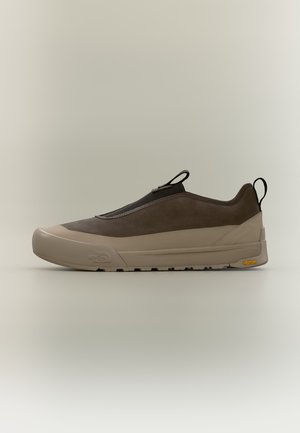 Brauner Slip-On-Sneaker mit beiger Sohle, schwarzen Zuglaschen und Vibram-Außensohle, seitlich vor neutralem Hintergrund dargestellt.