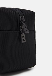 Čierna textúrovaná úložná taška so zipsom. Obsahuje dvojité čierne ťaháky na zips označené logom "B", kompaktný tvar kocky.