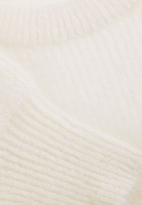 Weicher, weißer, gestrickter Stoff mit gerippten Mustern und einer glatten, flauschigen Textur.