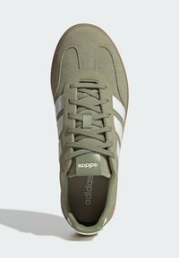 Zelene nubuk tenisice imaju dizajn s vezicama, bijele pruge i gumeni potplat. Istaknuti brend na jeziku i unutrašnjosti obuće.