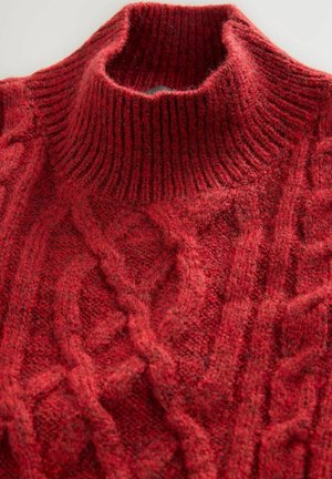 Röd stickad tröja med hög, ribbad polokrage och flätstickad design. Tyget verkar tjockt och texturerat, vilket ökar värmen.