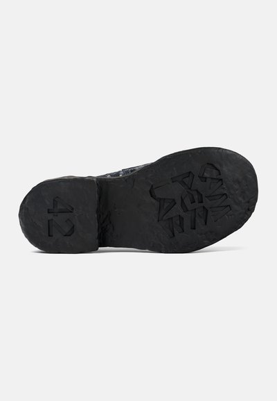 Black shoe outsole with textured, rugged surface and molded branding. Features raised patterns and indents for grip and traction. Size 42.