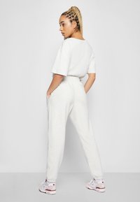 Completo sportivo grigio chiaro composto da una T-shirt larga e pantaloni con vita elastica dotati di tasche. Modello che indossa sneakers bianche e rosa.