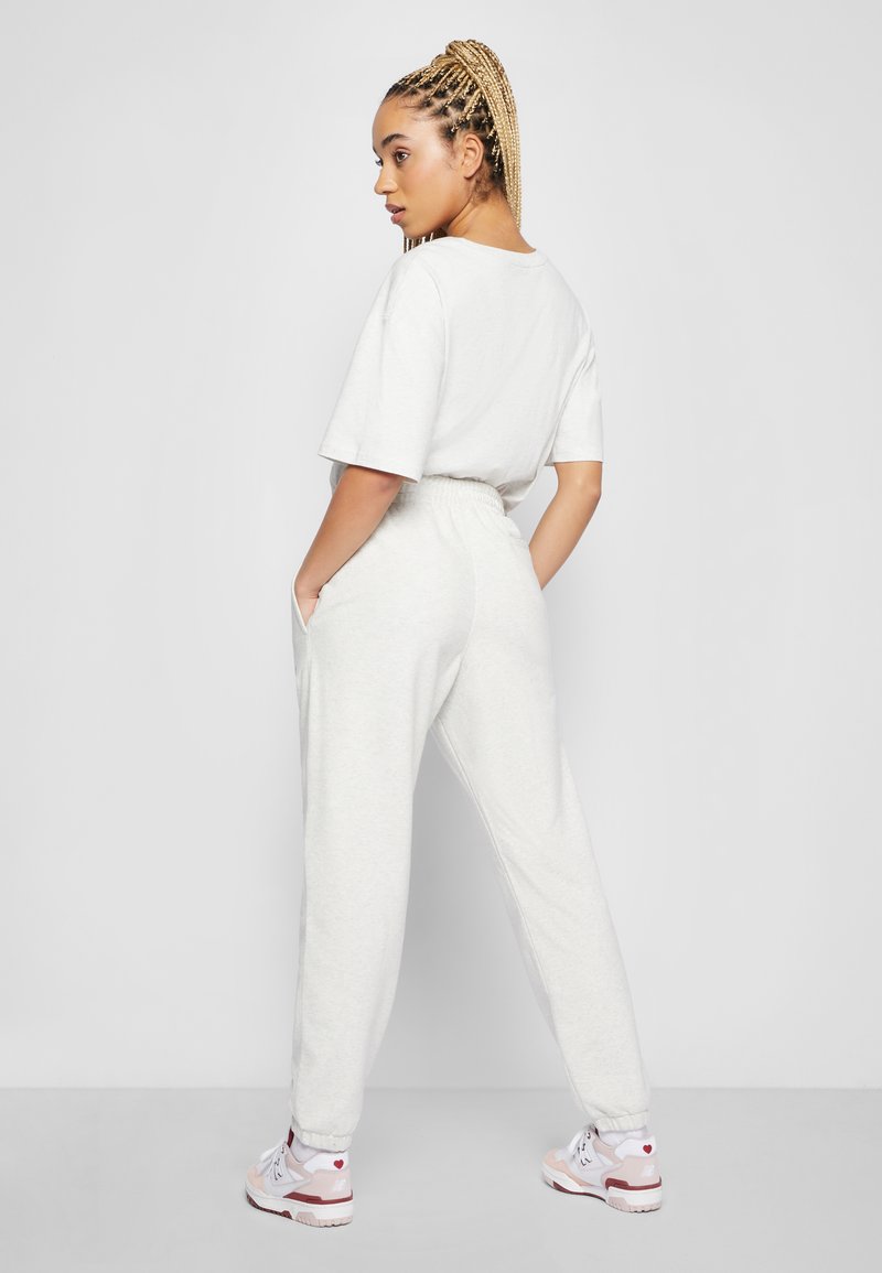 Ensemble de survêtement gris clair comprenant un T-shirt ample et un pantalon à taille élastique avec poches. Modèle portant des baskets blanches et roses.