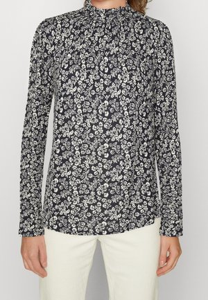 Blusa floreale blu navy con maniche lunghe e colletto alto, caratterizzata da schemi di fiori bianchi e una morbida trama del tessuto. L'orlo anteriore è leggermente più lungo.