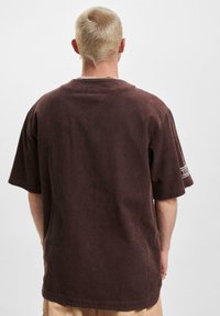 Camicia a maniche corte in velluto a coste marrone con una vestibilità rilassata; presenta una leggera texture a coste e una patch con logo sulla manica.