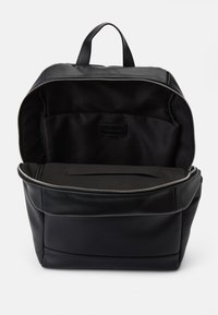 Sac à dos en cuir noir avec une ouverture zippée, offrant un intérieur spacieux et une poche plate. La texture est lisse avec une finition mate.