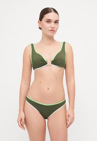 Olivenfarbener Bikini aus geripptem Material, mit breiten Trägern und kontrastierenden neongrünen sowie weißen Akzenten auf dem Oberteil und dem Unterteil.