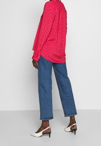 Camicia rosa con motivo a diamante, abbinata a jeans dritti blu e décolleté bianche.