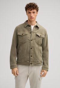 Giacca di jeans verde oliva con due tasche sul petto, chiusura a bottoni e taglio dritto. Tessuto strutturato con dettagli di cucitura visibili.