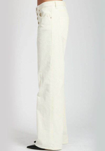 Pantaloni a palazzo a righe verticali bianchi con cinque bottoni davanti, tessuto texturizzato e tasche laterali. Indossati con tacchi neri a punta.