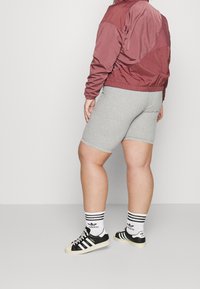 Kastanjefärgad kort jacka, grå shorts, svarta Adidas-sneakers med tre ränder och matchande randiga strumpor. Slät tyg och figursydd design.