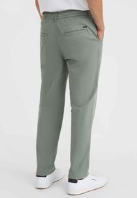 Lichtgroene, relaxte broek met een elastische tailleband, twee achterzakken en zijnaad, gecombineerd met witte sneakers.
