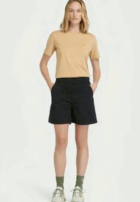 Light beige t-shirt and navy shorts. The shorts have a relaxed fit with pockets, paired with green socks and beige shoes.