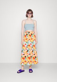 Top curto azul claro combinado com uma saia longa floral com padrões em laranja, rosa e verde. Usado com sandálias roxas de tiras.