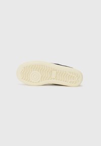 Fekete sneaker, textúrált talppal, fehér gumitalppal és hullámmintázattal. A design minimalista stílust tükröz.