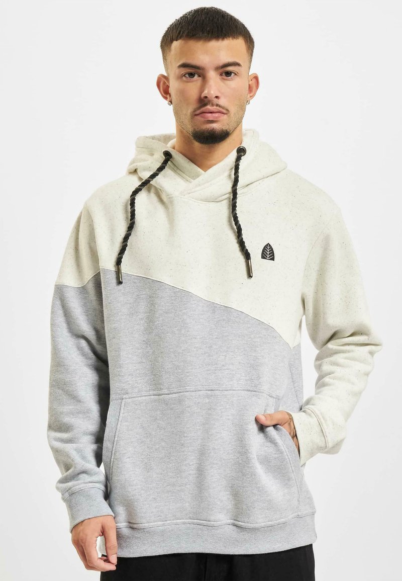 Hooded sweatshirt in cream and light gray, featuring a split design, speckled texture, drawstring accents, and a small leaf logo.