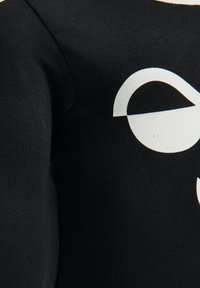 Zwarte sweatshirt met een grote witte grafische ontwerp. De stof lijkt zacht met een gestructureerde afwerking, wat een gedurfde visuele tegenstelling benadrukt.