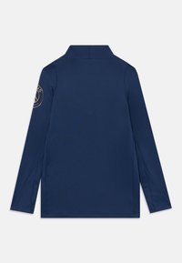 Laivastonsininen pitkähihainen polo pystykauluksella, jossa on kultainen emblem vasemmassa hihassa. Sujuva kangas ja lievät halkiot helmassa.