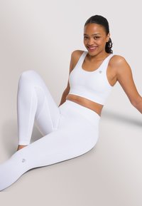 Set atletico bianco composto da un reggiseno sportivo a costine e leggings coordinati. Il tessuto ha una texture morbida, con un logo in evidenza sul petto e sulla gamba.
