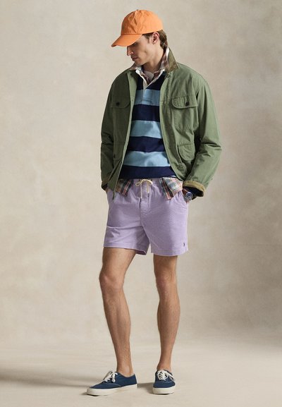 Πράσινο βαμβακερό μπουφάν πάνω από μπλε και γαλάζια ριγέ πουλόβερ, καρό πουκάμισο, μωβ ριγέ σορτς και μπλε αθλητικά παπούτσια, ολοκληρωμένα με πορτοκαλί καπέλο.