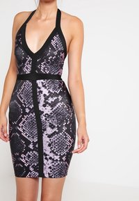 Dámské bodycon šaty s potiskem černé a fialové hadí kůže, s halter výstřihem, černými ramínky a pevným černým pasem. Hladký materiál a těsně přiléhající střih.