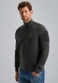Grauer Rollkragenpullover aus Strickmaterial, mit einem strukturierten Rippkragen und einem schwarzen Stoffpatch auf der linken Schulter.