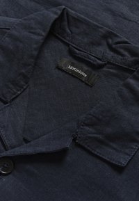 Camisa de lino azul marino con un cuello plano, un cierre de un solo botón y una etiqueta con el nombre de la marca "Matinique". Textura suave.