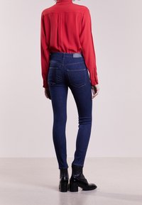 Červená blůza s dlouhým rukávem spárovaná s tmavě modrými skinny džíny. Džíny mají vysoký pas, pět kapes a decentní švy. Černé kotníkové boty.