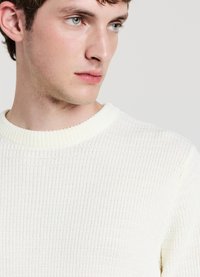 Maglione beige chiaro a costine con scollo rotondo, che mette in risalto un tessuto strutturato e una sottile lucentezza. Focus sui dettagli di scollo e spalle.