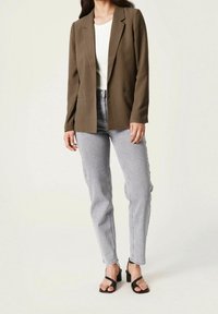 Olivově zelený blazer se zářezovými klopami, kombinovaný s bílým žebrovaným topem a světle šedými vysokým pasem džínami, doplněný černými řemínkovými podpatky.