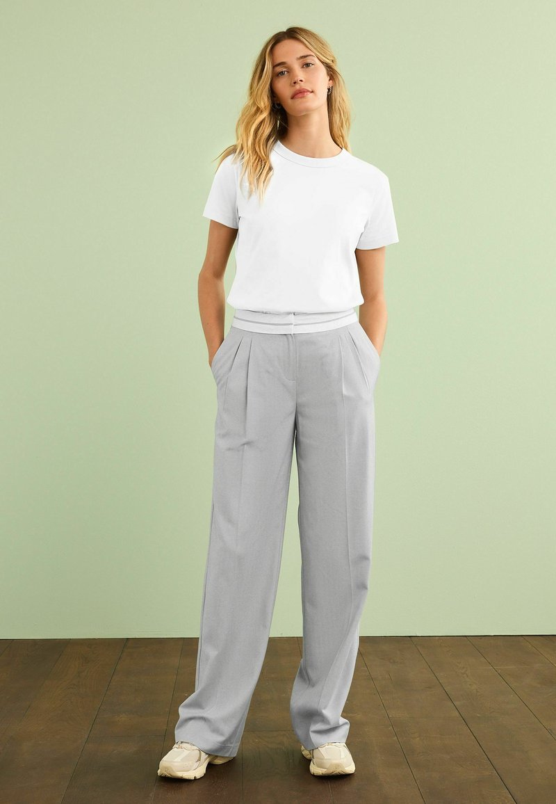 White short-sleeve t-shirt paired with light gray, high-waisted, wide-leg pants. Pants feature front pleats and side pockets, styled with beige sneakers.