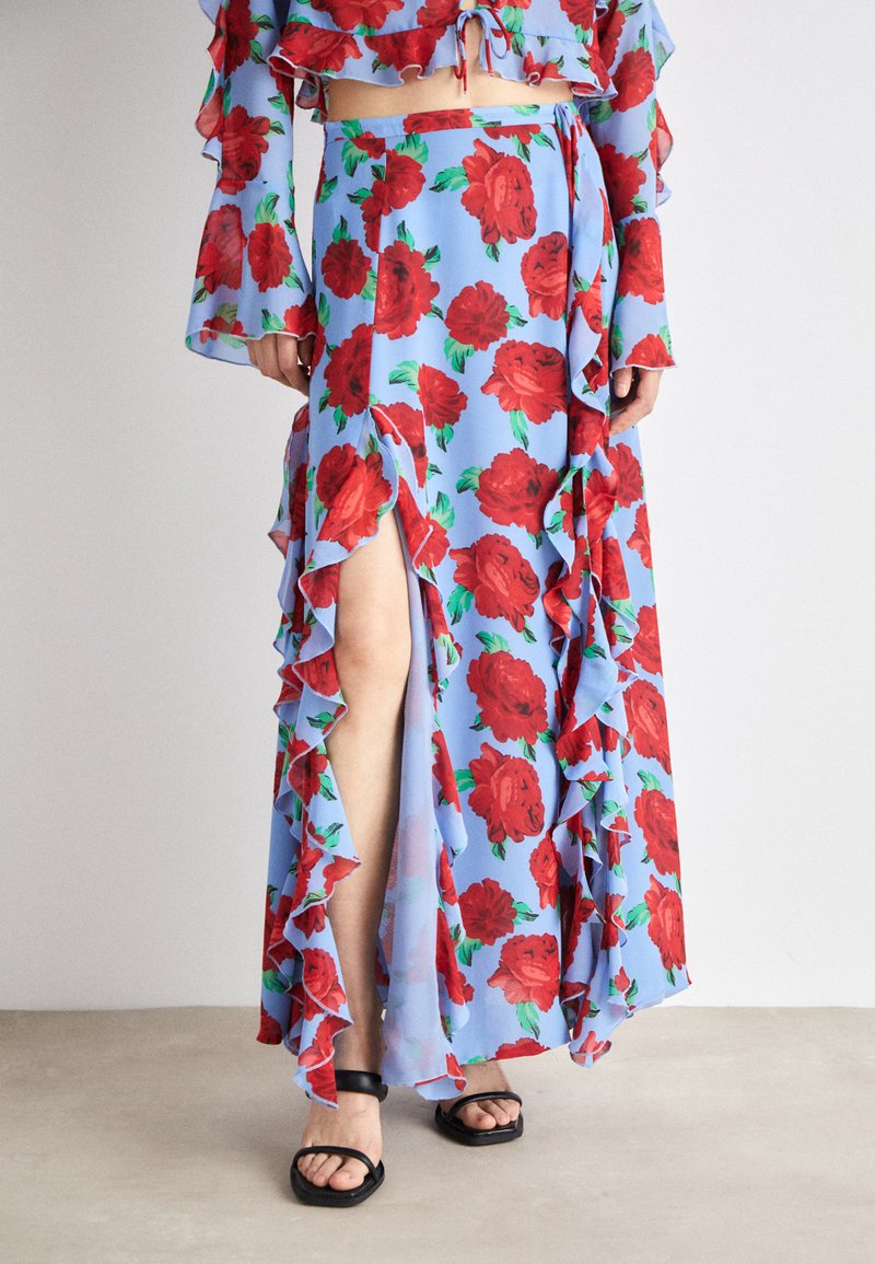 Dress in light blue fabric with a red rose pattern, featuring ruffled edges and a thigh-high slit. Paired with black sandals.