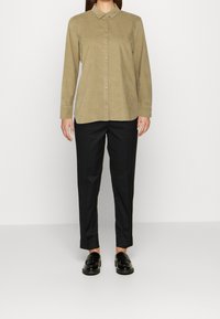 Camisa khaki de botones con cuello, combinada con pantalones negros ajustados y mocasines negros, creando un look simple y limpio.
